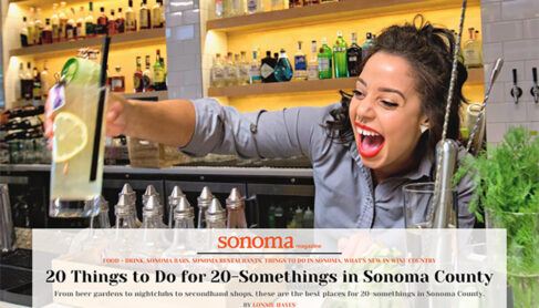 A happy and smiling female bartender at Perch + Plow handing a handcrafted cocktail to a customer with text overlay "Sonoma Magazine 20 Things to do for 20-something in Sonoma County"