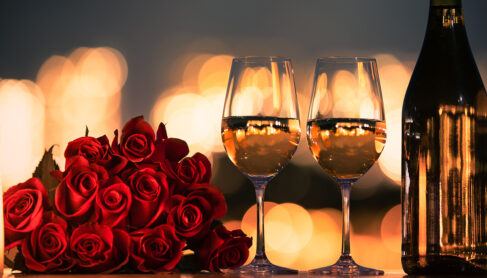 Romantic dinner date night with roses and wine on the table and city lights in the background.